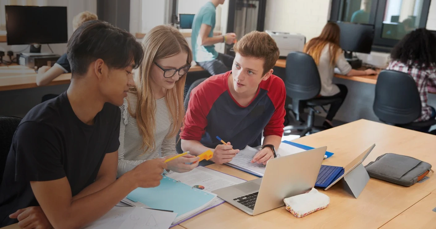 Zwei Schüler und eine Schülerin sitzen vor Arbeitsmaterial und unterhalten sich
